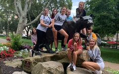 A group of campers gathered around a Pitt Panther as they have fun around campus